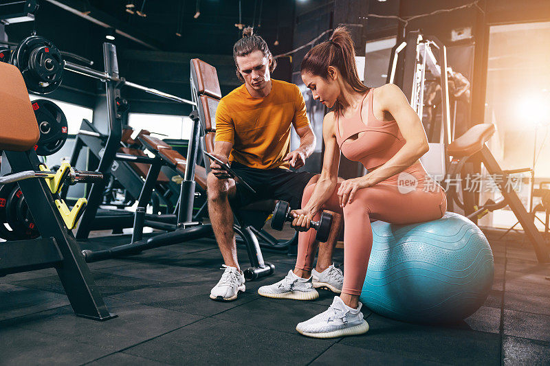 运动女子训练肌肉的私人类健身房与私人教练的帮助支持