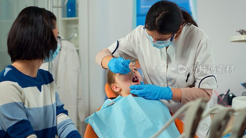 戴着口罩的儿科牙医为小女孩病人治疗牙齿