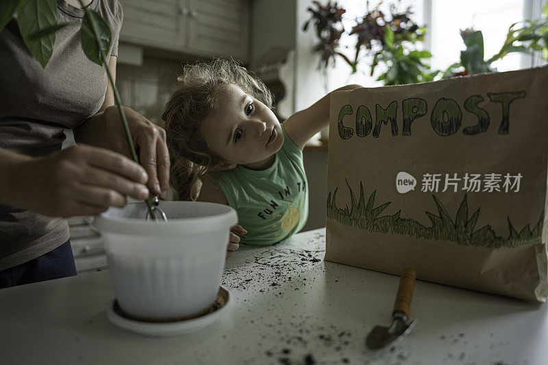 女孩和妈妈一起用堆肥重新盆栽植物。