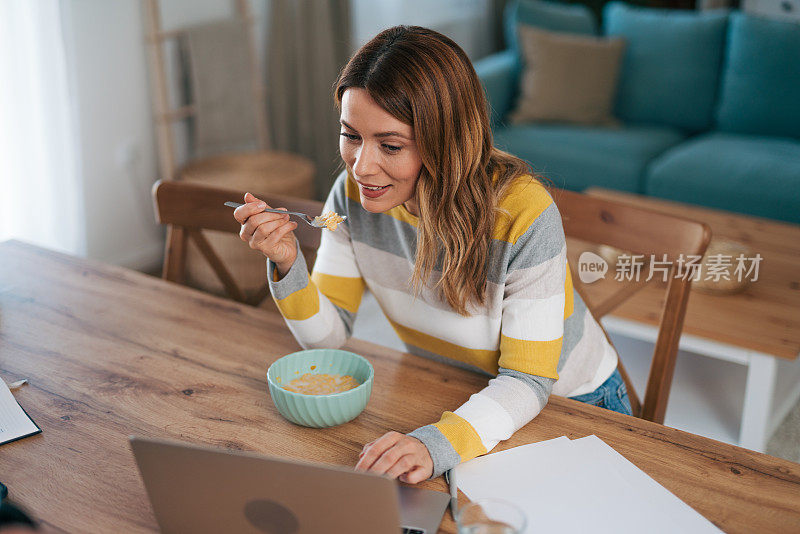 一个面带微笑的女人一边打视频电话一边吃早餐。