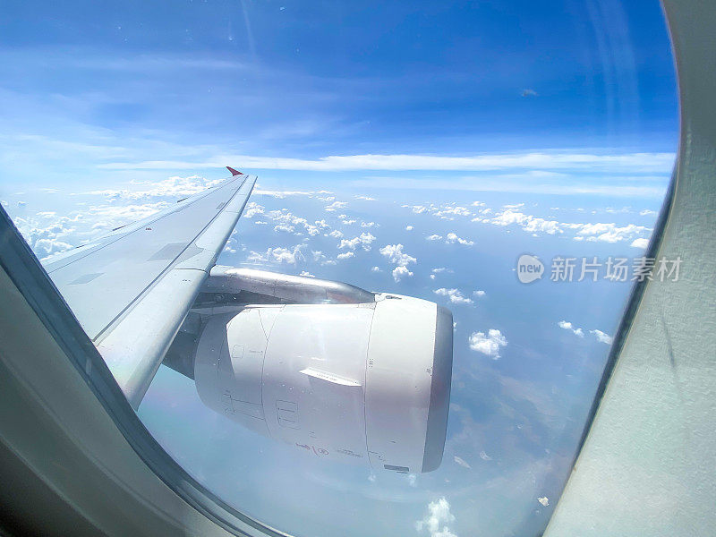 透过窗户看飞机在机翼飞行与一个美丽的蓝天和云。飞机窗外的景色。白天阳光灿烂的白天。旅游和独自旅行的概念。