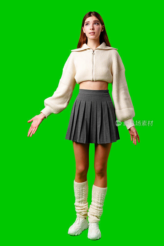 一个女人穿着裙子和毛衣站在绿色的屏幕背景上。她看起来泰然自若，直视着镜头。