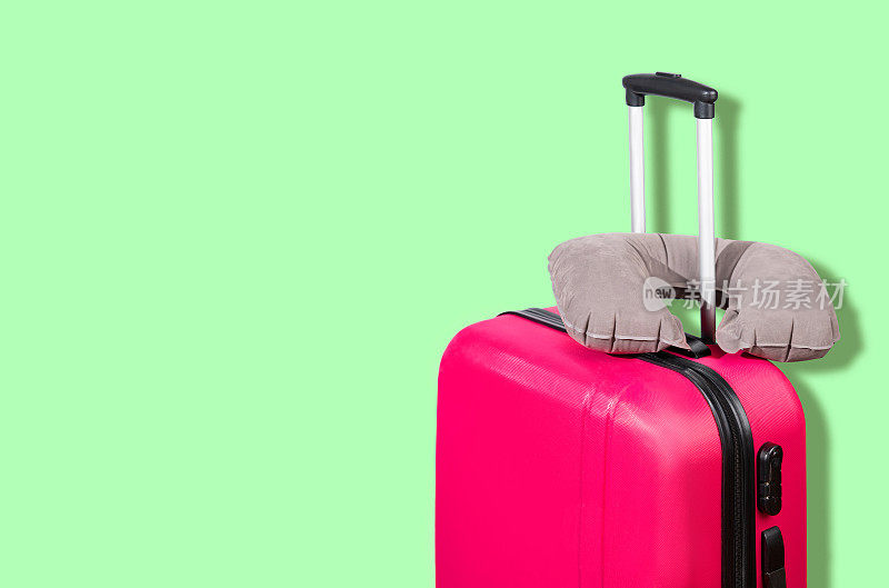 绿色背景上的粉色行李箱和灰色旅行枕头。