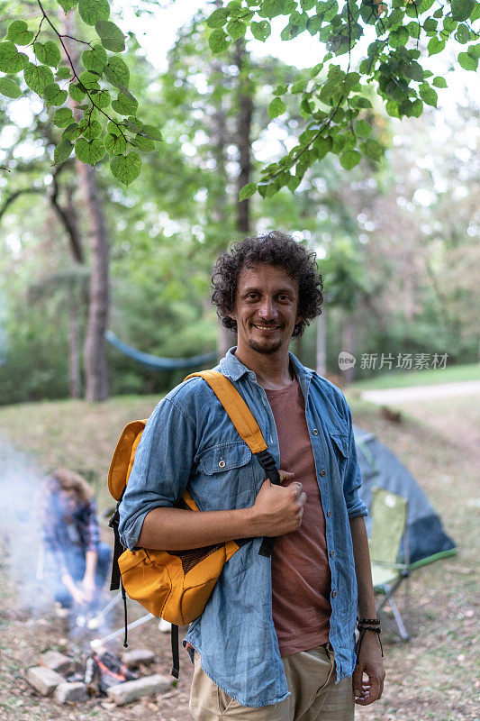 一个微笑着的年轻人和他的朋友们在森林里露营的照片