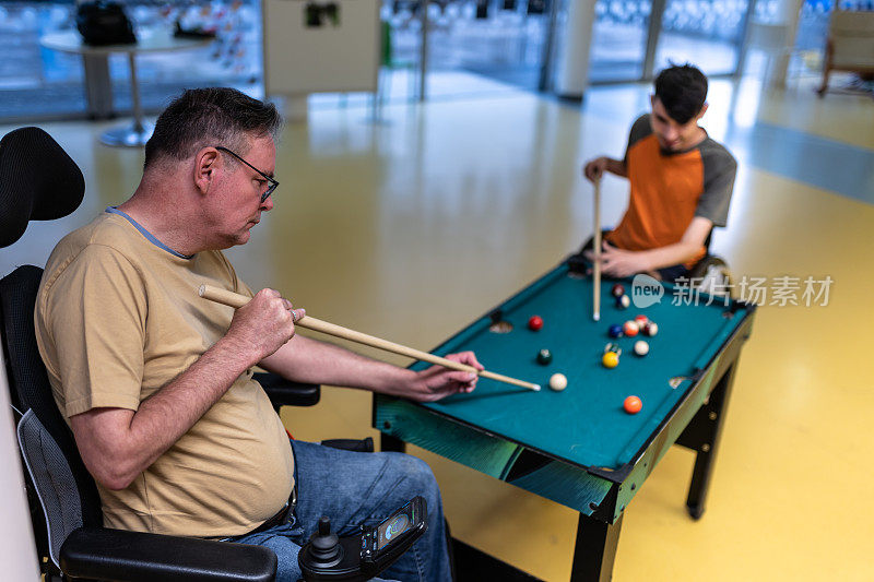 两个残疾人坐在轮椅上玩台球和桌上足球