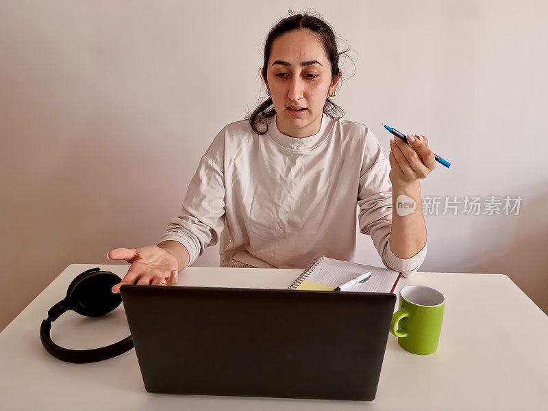 漂亮的年轻女子在家里用笔记本电脑和ipad，戴着耳机和一杯饮料