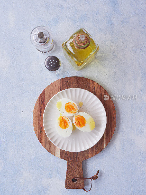 从上面开始，把两个煮熟的鸡蛋加橄榄油和胡椒粉放在一个白色盘子里，放在一个圆形的木制砧板上。