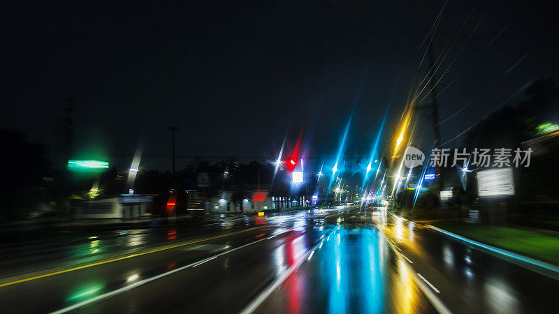 夜间暴雨后驾车。在潮湿的道路上行驶。散焦光迹与软焦点，镜头光晕