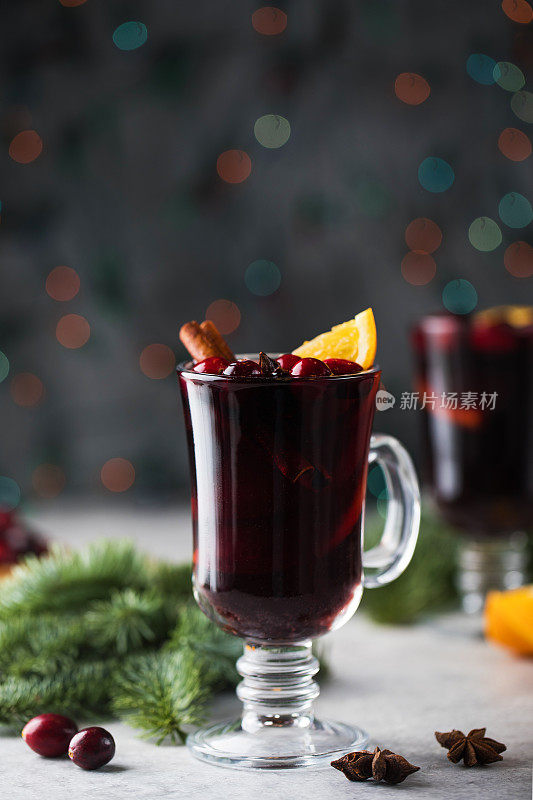玻璃杯里放着自制的热葡萄酒，圣诞背景是圣诞树的树枝、蔓越莓和散景。