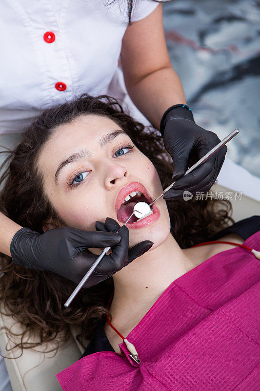 牙医在牙科诊所检查一位年轻女病人的牙齿。牙科的概念。牙科诊所里的牙医和病人。
