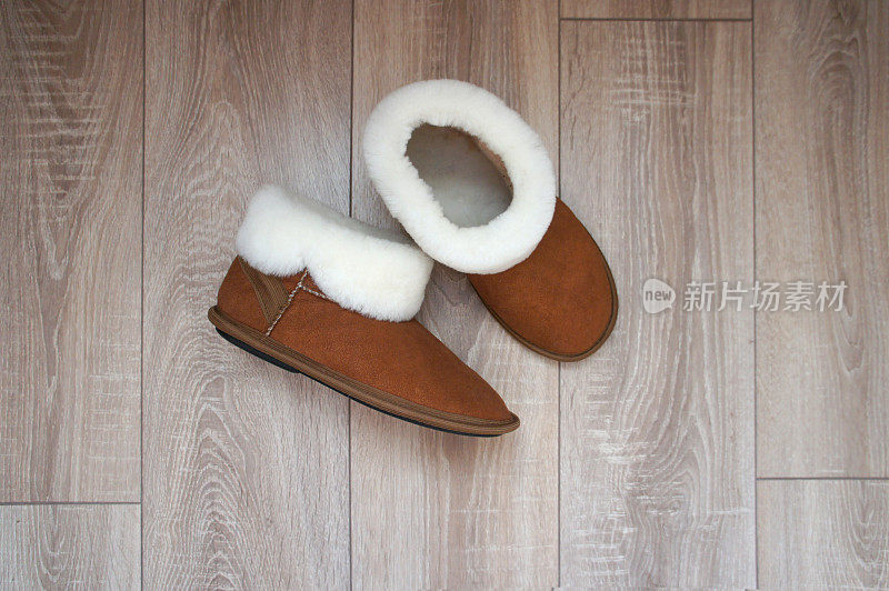 白色毛皮的棕色雪地靴。家里的拖鞋放在房间的镶木地板上。