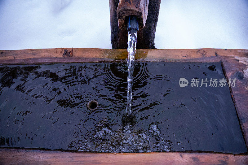 特写镜头:一股水流从天然泉水流入牛槽的木槽。水和气泡的运动