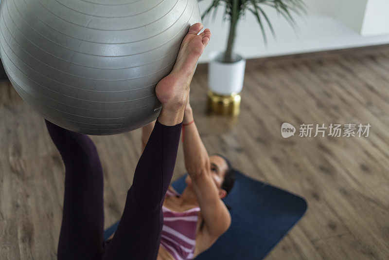 一位拉丁妇女坐在家里的客厅里，拿着她的瑜伽垫做着每天的练习