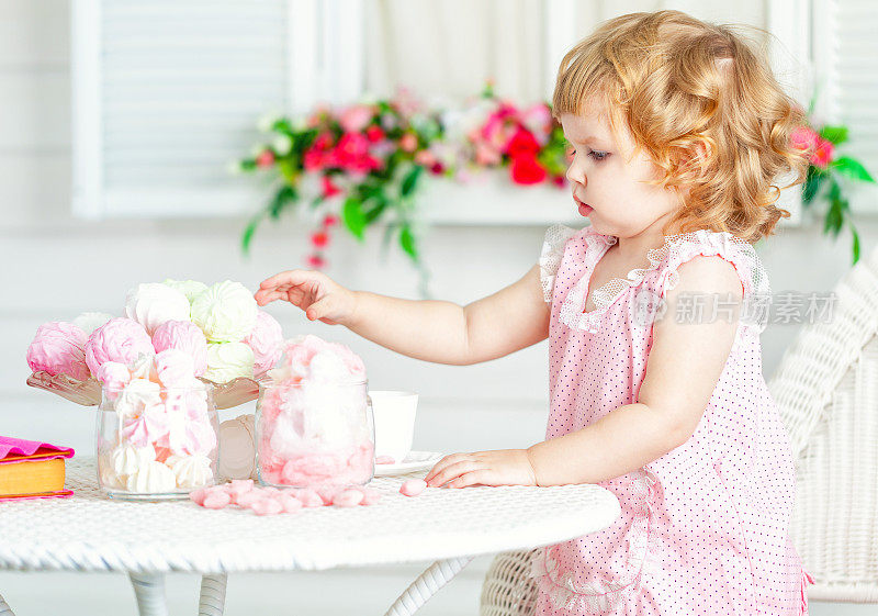 可爱的卷发小女孩穿着粉红色的裙子吃不同的糖果。