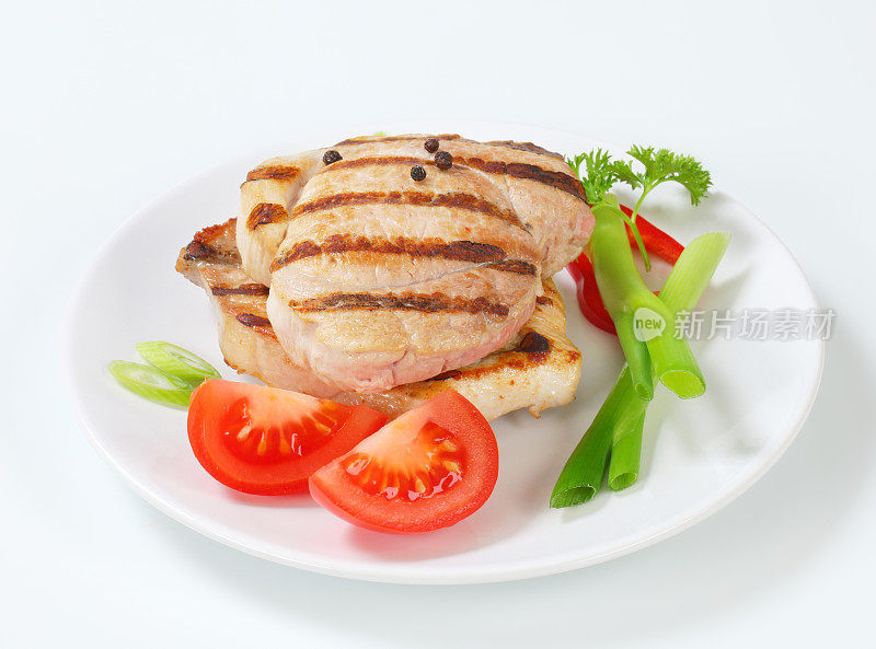用蔬菜装饰的烤猪肉排放在盘子里