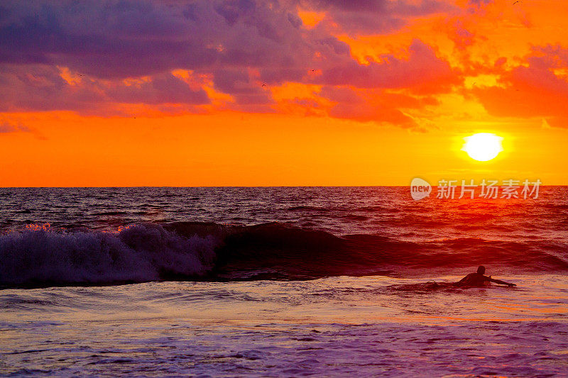 哥斯达黎加，冲浪者在夕阳下等待海浪