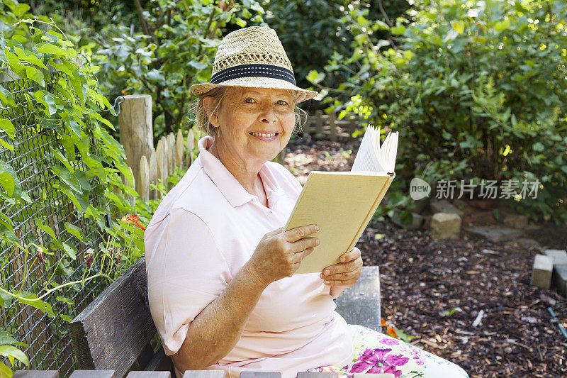 老妇人在花园里的长凳上阅读纸质书