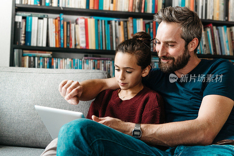 留胡子的父亲和女儿在沙发上敲打着平板电脑