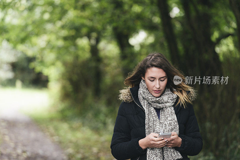 一个年轻女子在树林里用手机发短信。