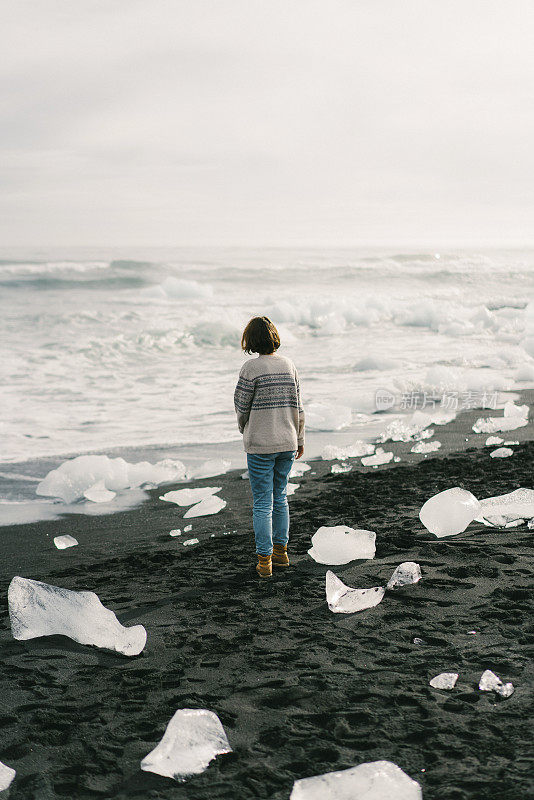 在Jokulsarlon附近被冰山覆盖的海滩上行走的女人