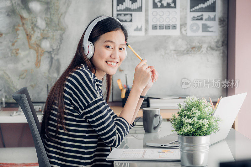 年轻的亚洲休闲女商人手臂上的桌子休息姿势与笔记本电脑和听音乐通过耳机思考工作，工作在家里与放松的感觉概念