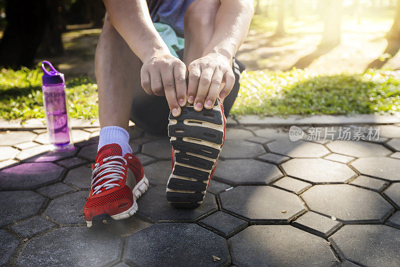 亚洲运动员在公园的道路上跑步前伸展他的双腿。跑步是为了减肥和健康