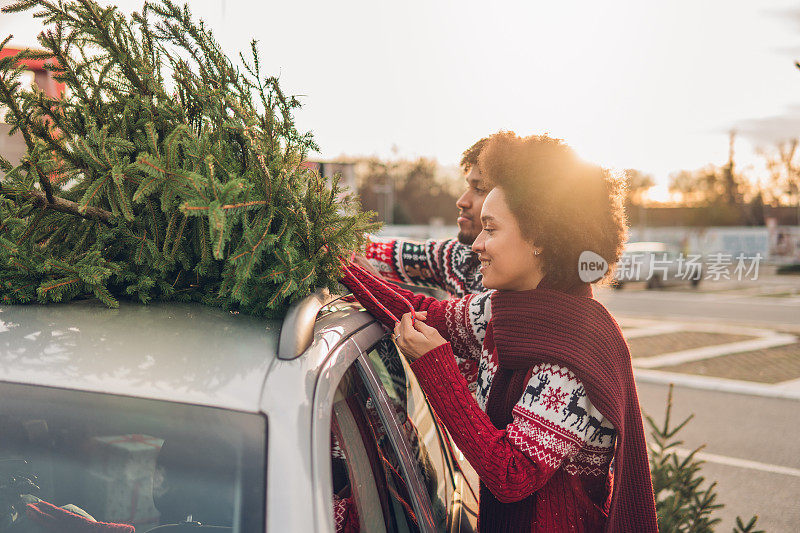 快乐的男人和女人把圣诞树绑在车上