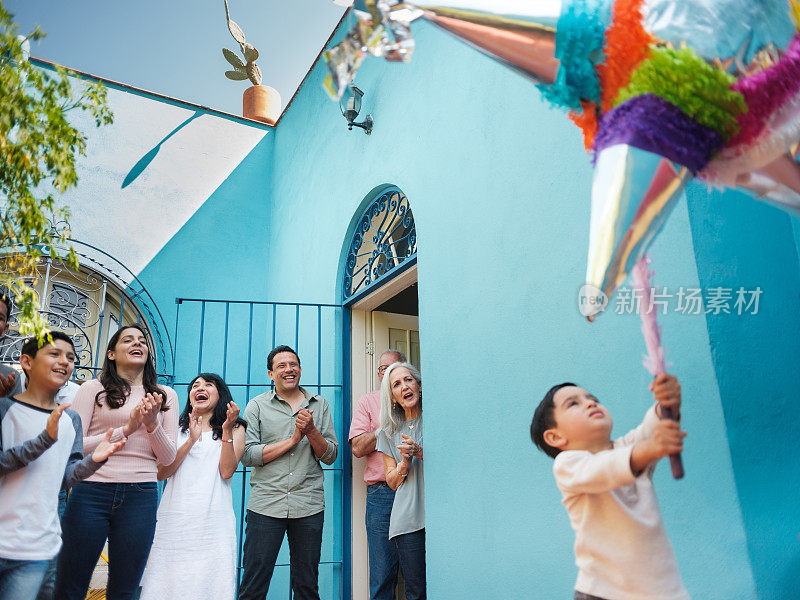 墨西哥小男孩打piñata，家人在后面鼓掌