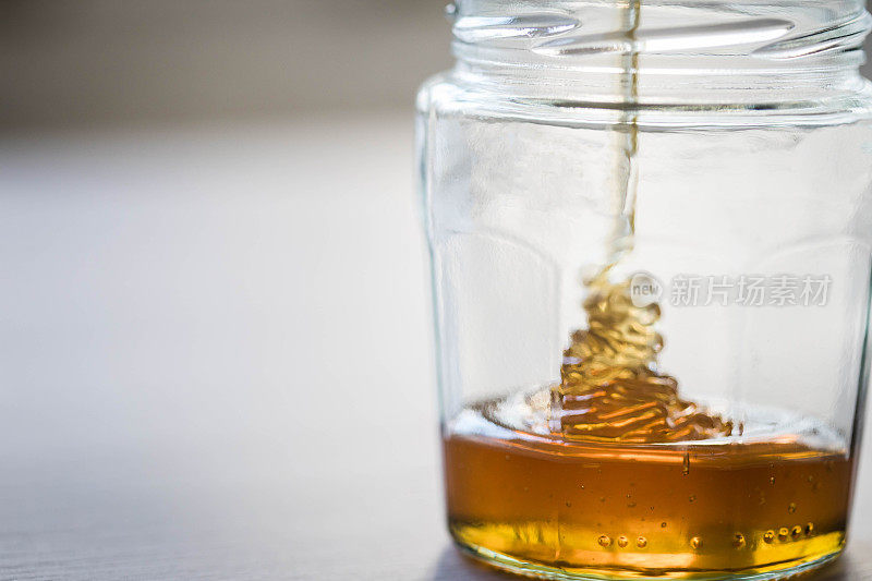 蜂蜜从玻璃罐里的蜂蜜勺中滴落。