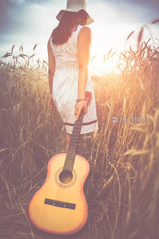 拿着吉他的女人走过高高的草丛。