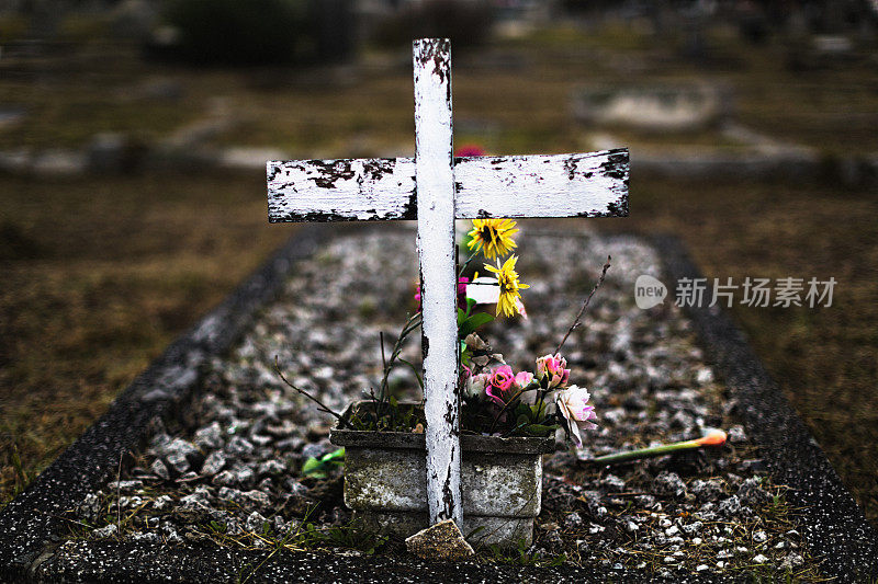 简陋的坟墓上有饱经风霜的木十字架，鲜花盛开，看起来很凄凉