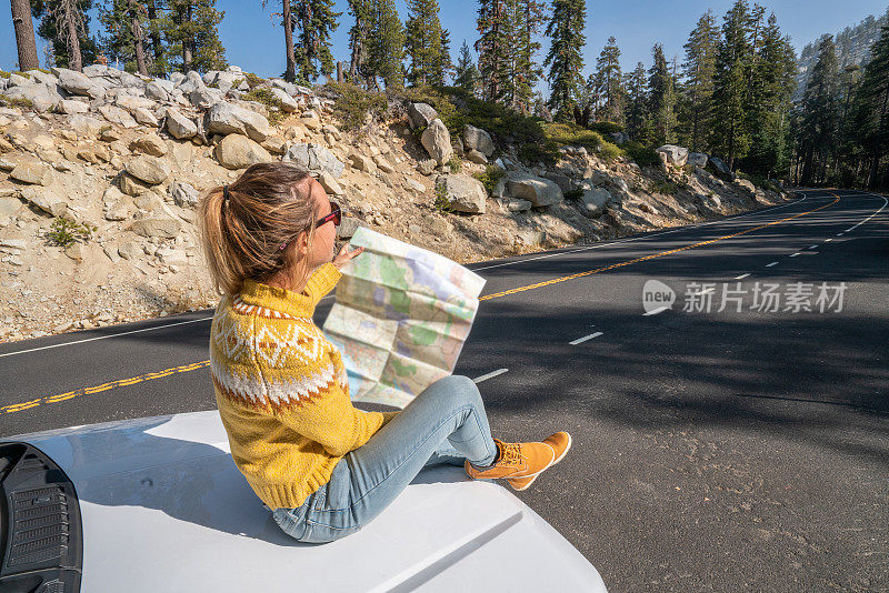 公路旅行概念;女人坐在汽车引擎盖上查看路线图