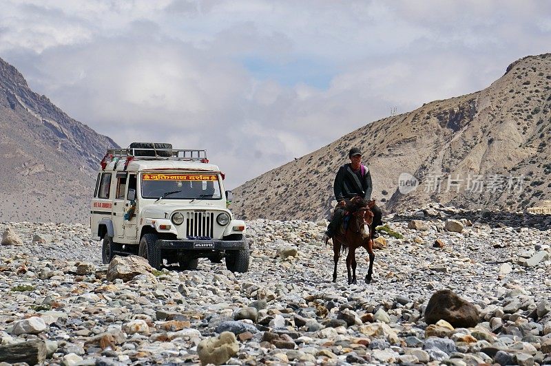 一辆旅游吉普车和一个当地居民骑着马在喜马拉雅山脉中前往上野马