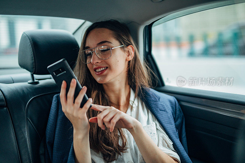 女商人坐在汽车后座上使用智能手机