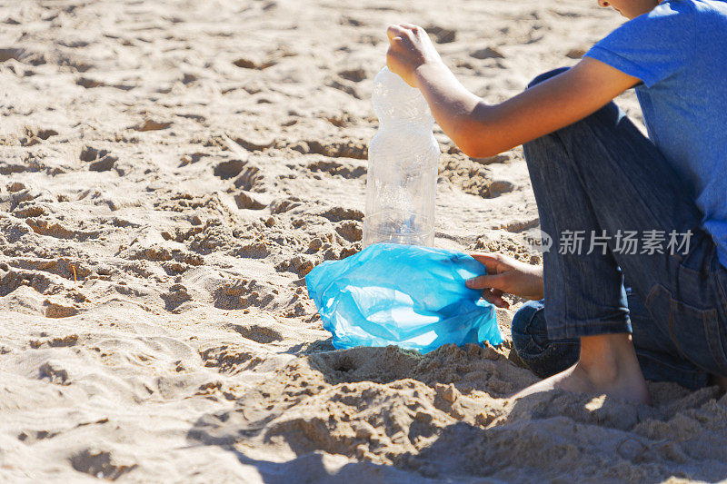 清理海滩上的塑料垃圾。用手从沙子里捡起塑料瓶，放进塑料袋回收
