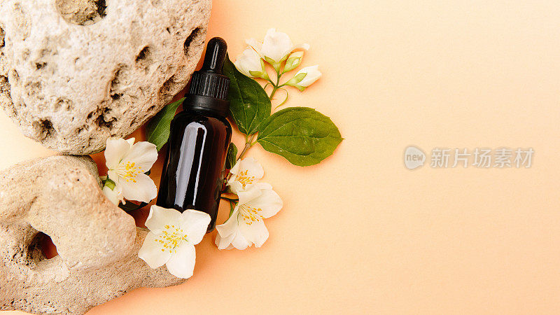漂亮的茶油组合。玻璃化妆品瓶立在一块石头上，米色的背景上有茉莉花，明亮的阳光。天然化妆品概念，天然精油。