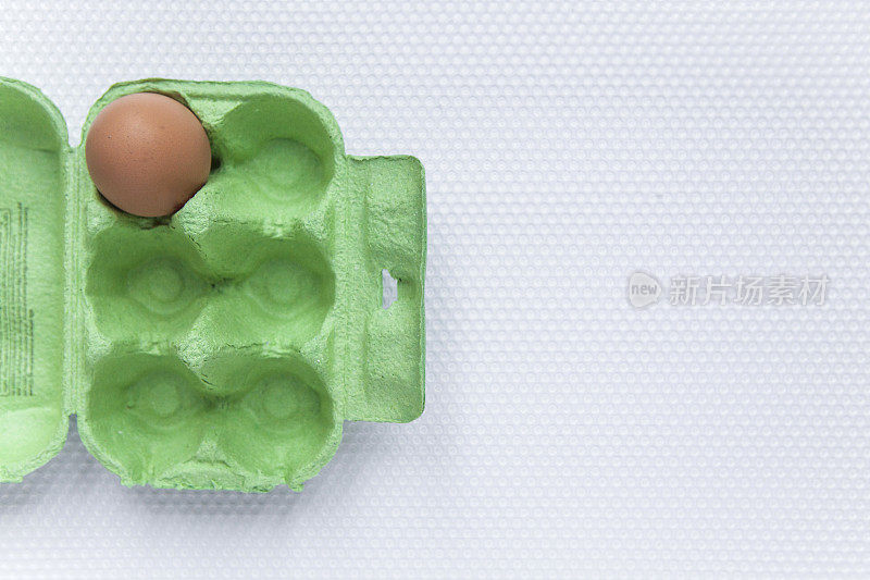一个鸡蛋在一个绿色的纸板鸡蛋盒上的塑料窝纹理表面直接观察与复制空间