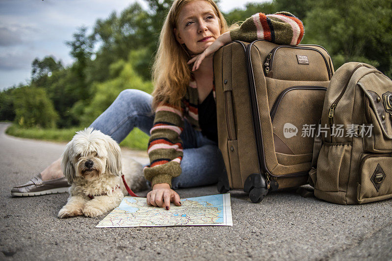 一个小女孩坐在一个手提箱旁边，抚摸着她的狗