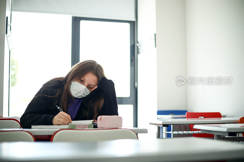 戴面具的女学生在教室里学习，带着新常态回到学校