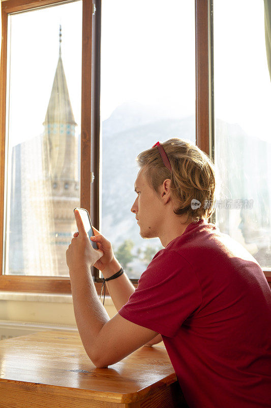 日出时，坐在窗台边的年轻人用手机发短信