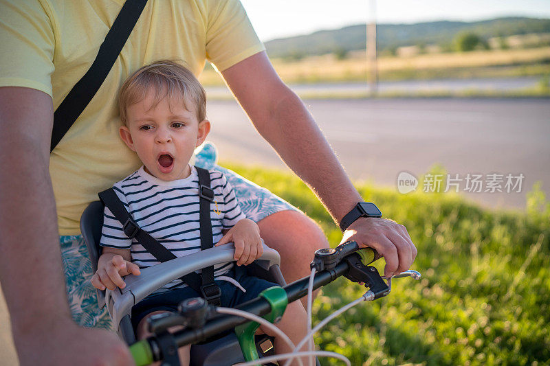 父亲骑着自行车，儿子坐在婴儿座椅上