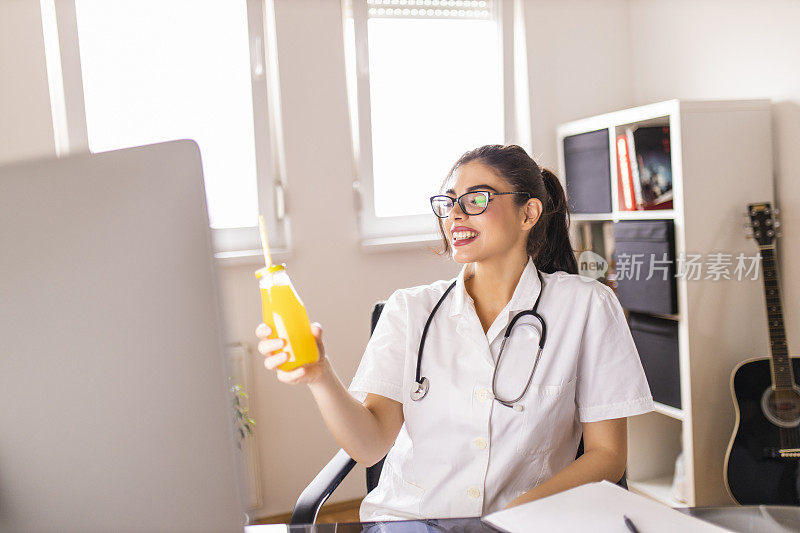 美丽的女医生在办公室工作，喝着橙汁
