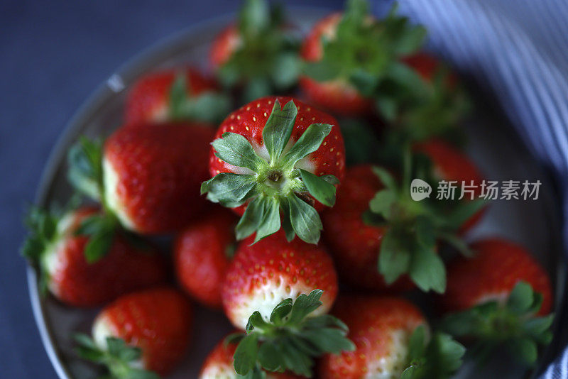 新鲜草莓在灰色盘子上，在深蓝色的混凝土背景，旁边是灰白色条纹布餐巾，特写