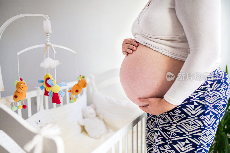 孕妇站在婴儿床旁摸肚子