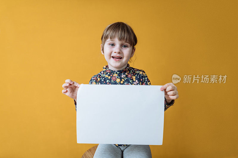 工作室肖像微笑四岁的女孩拿着空白的纸拷贝空间客户的信息