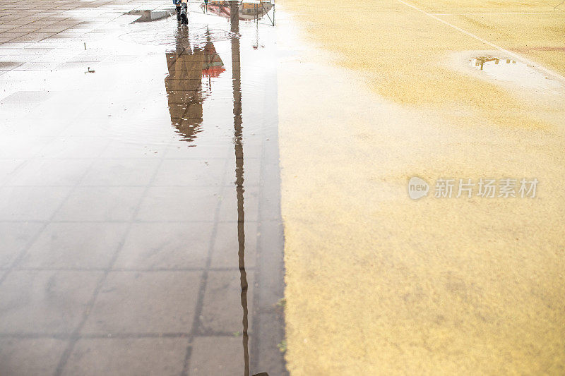 在城市中行走的女人的雨水坑里的倒影