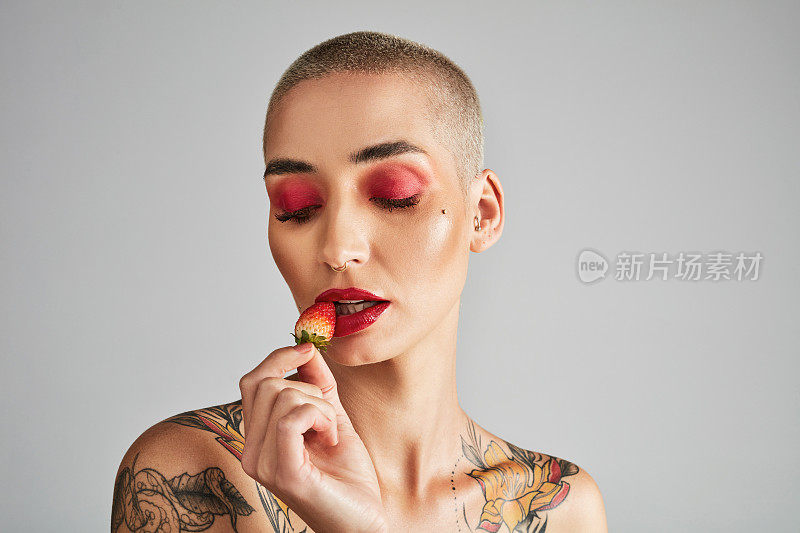 一个美丽的年轻女子在灰色背景下吃草莓的照片