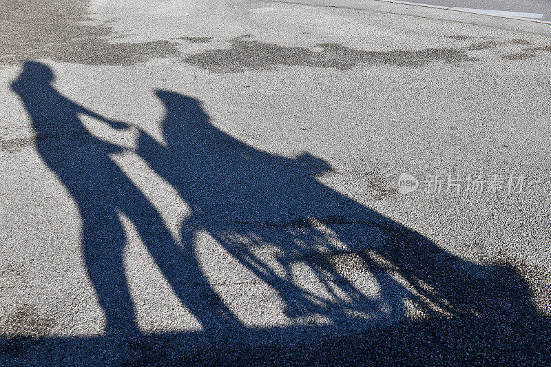 一个女人的影子驾驶在轮椅上的老人，沥青背景