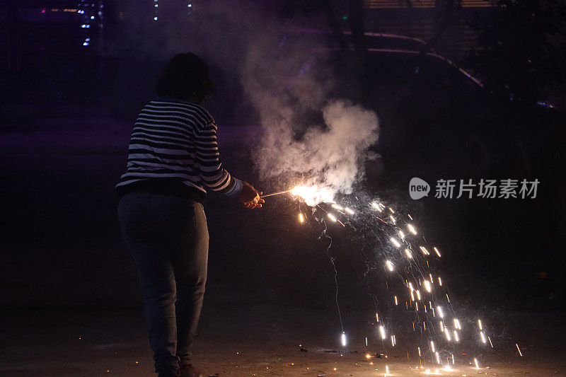 特写图像的印度妇女穿着休闲服装，拿着点燃的烟花庆祝排灯节，印度节日的烟花和烟花，后视镜