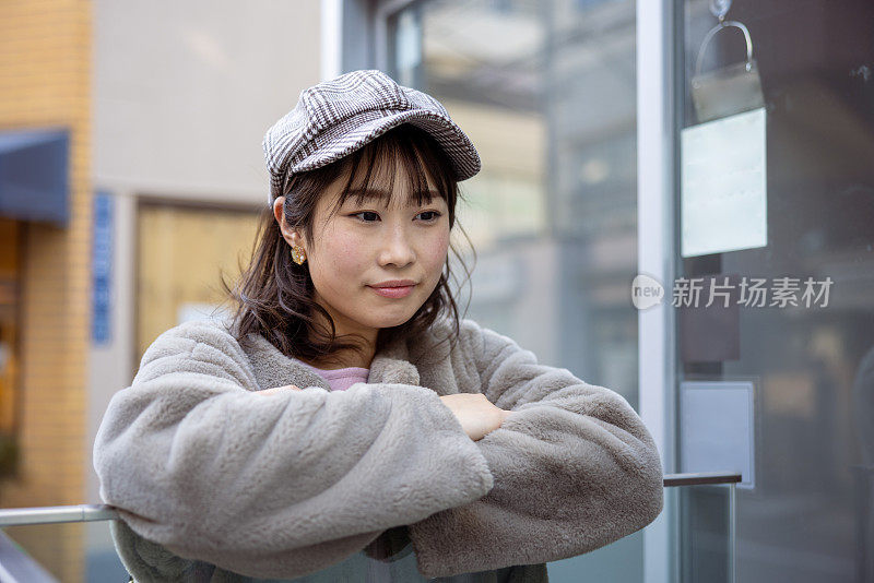 一个日本女人倚在玻璃墙上，在街上放松